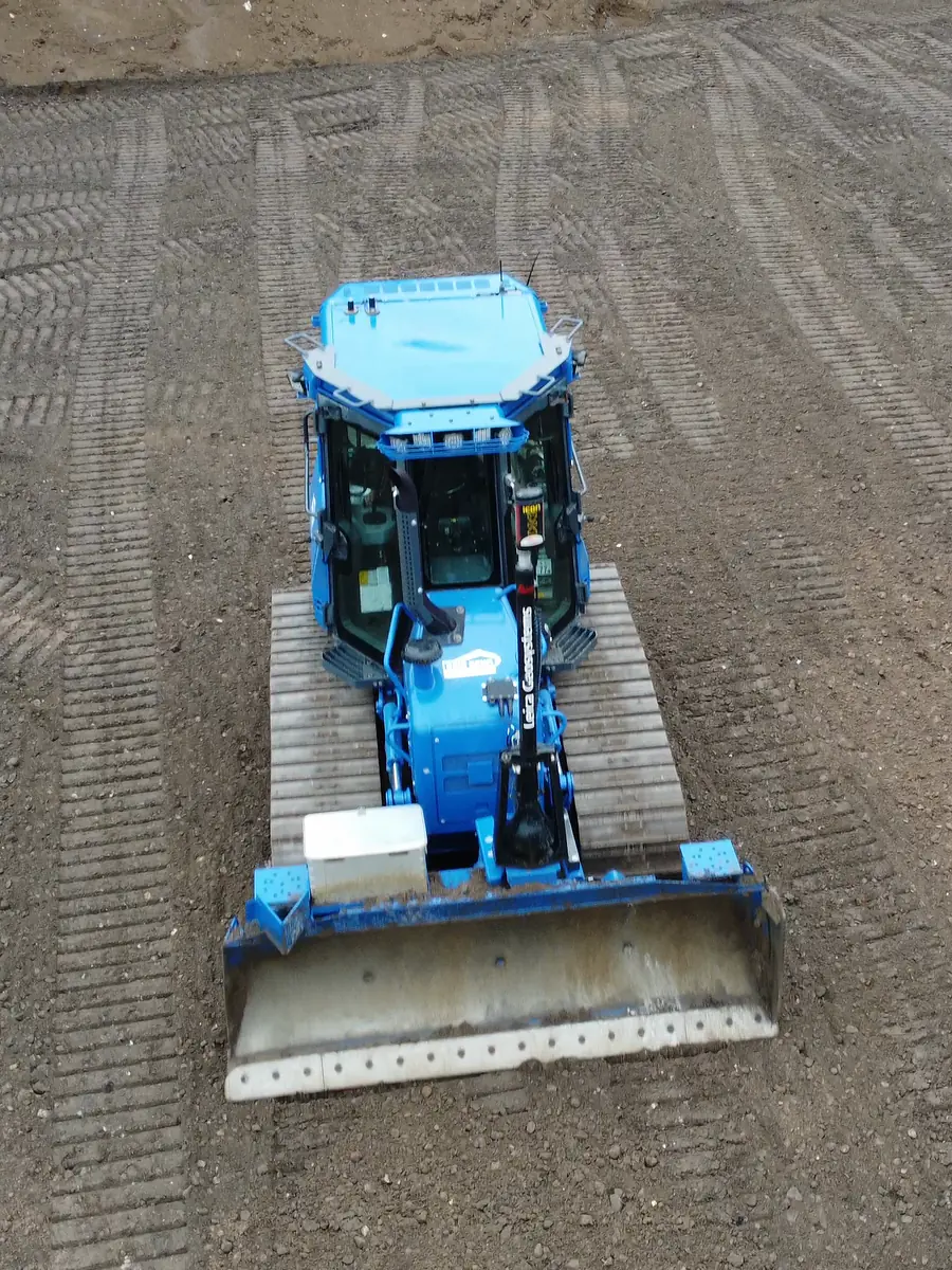Blaue 9-t-Planierraupe senkrecht von oben beim Schieben von Recyclingmaterial in Neuengörs, ringsum Kettenspuren