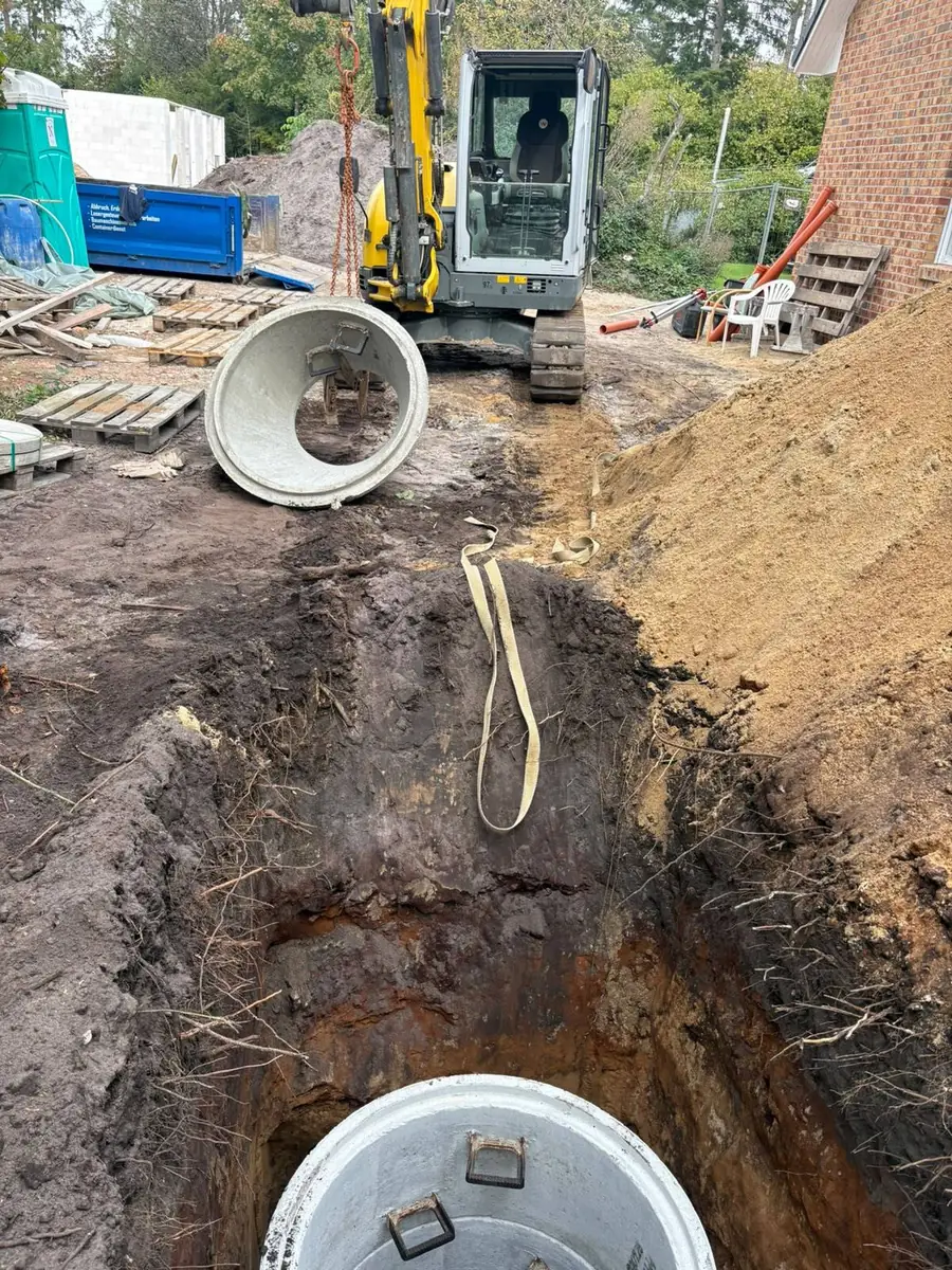 Kettenbagger von Erik Rehn hebt einen Betonschachtring an der Kette zur Baugrube des Sickerschachts in Norderstedt